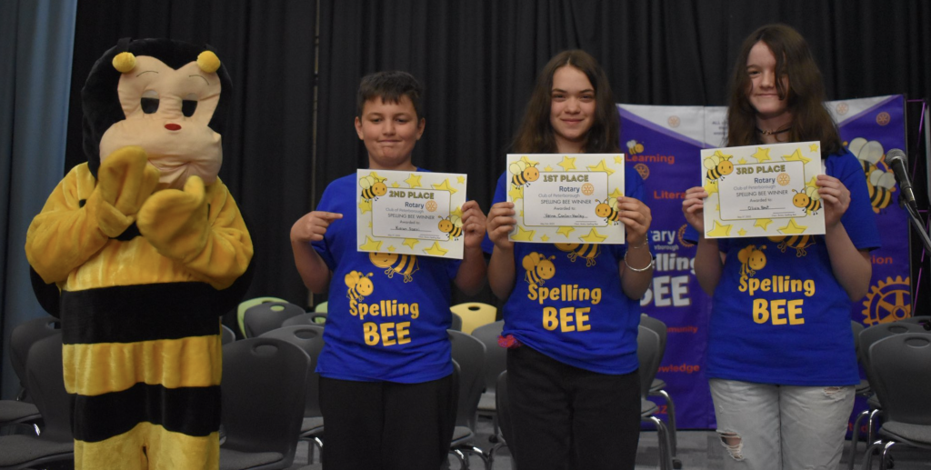 Three students hold certificates after participating in a Spelling Bee.